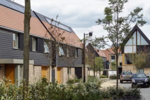 Timber cladding, gable ends, a pedestrian focused public realm and generous planting all give an informal, rural character to this neighbourhood at Abode, Great Kneighton, Cambridge.